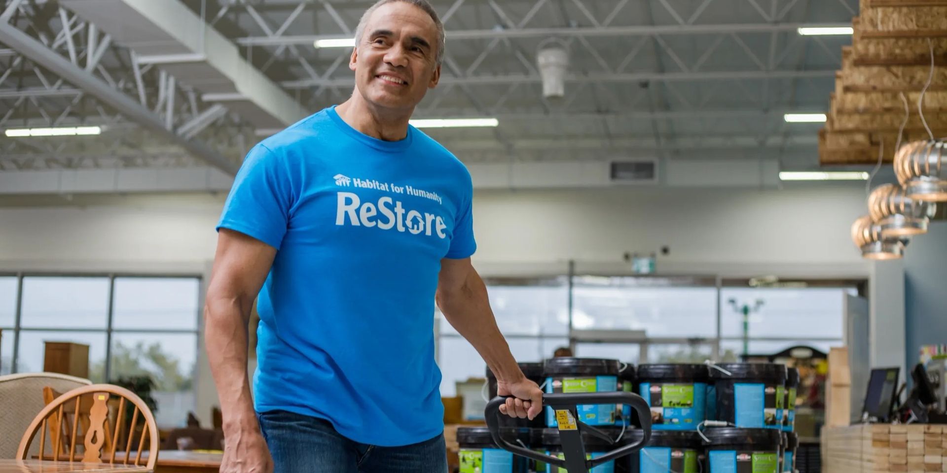 Habitat for Humanity New Brunswick volunteer in blue ReStore shirt standing beside a cart in a bright warehouse-like Restore