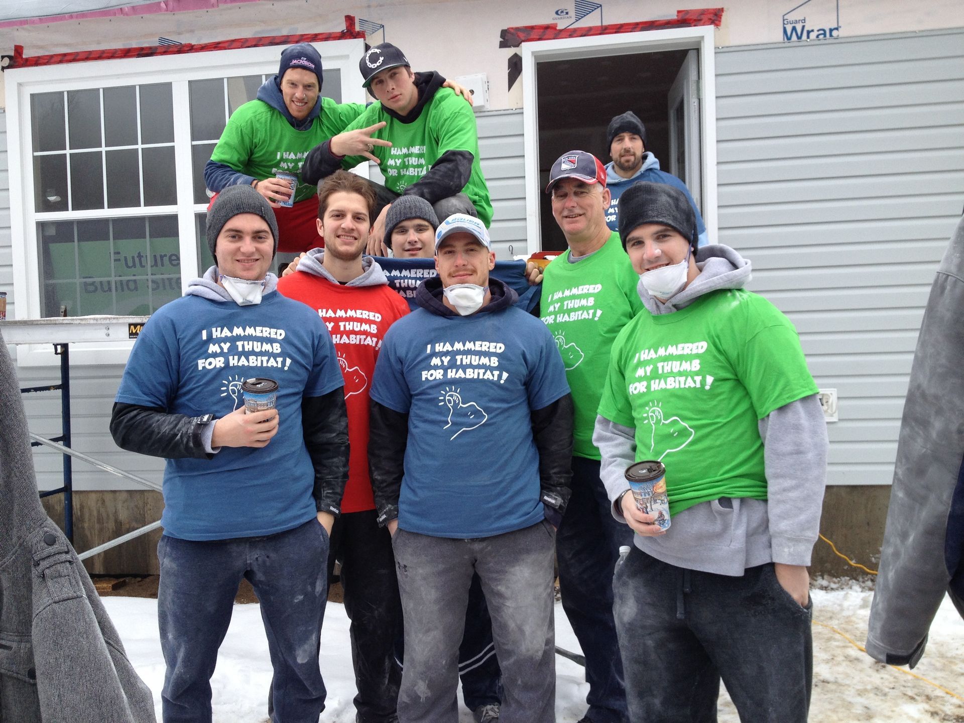 Group of Habitat New Brunswick volunteers in winter hats and masks posing outside a house, some holding paint cans.