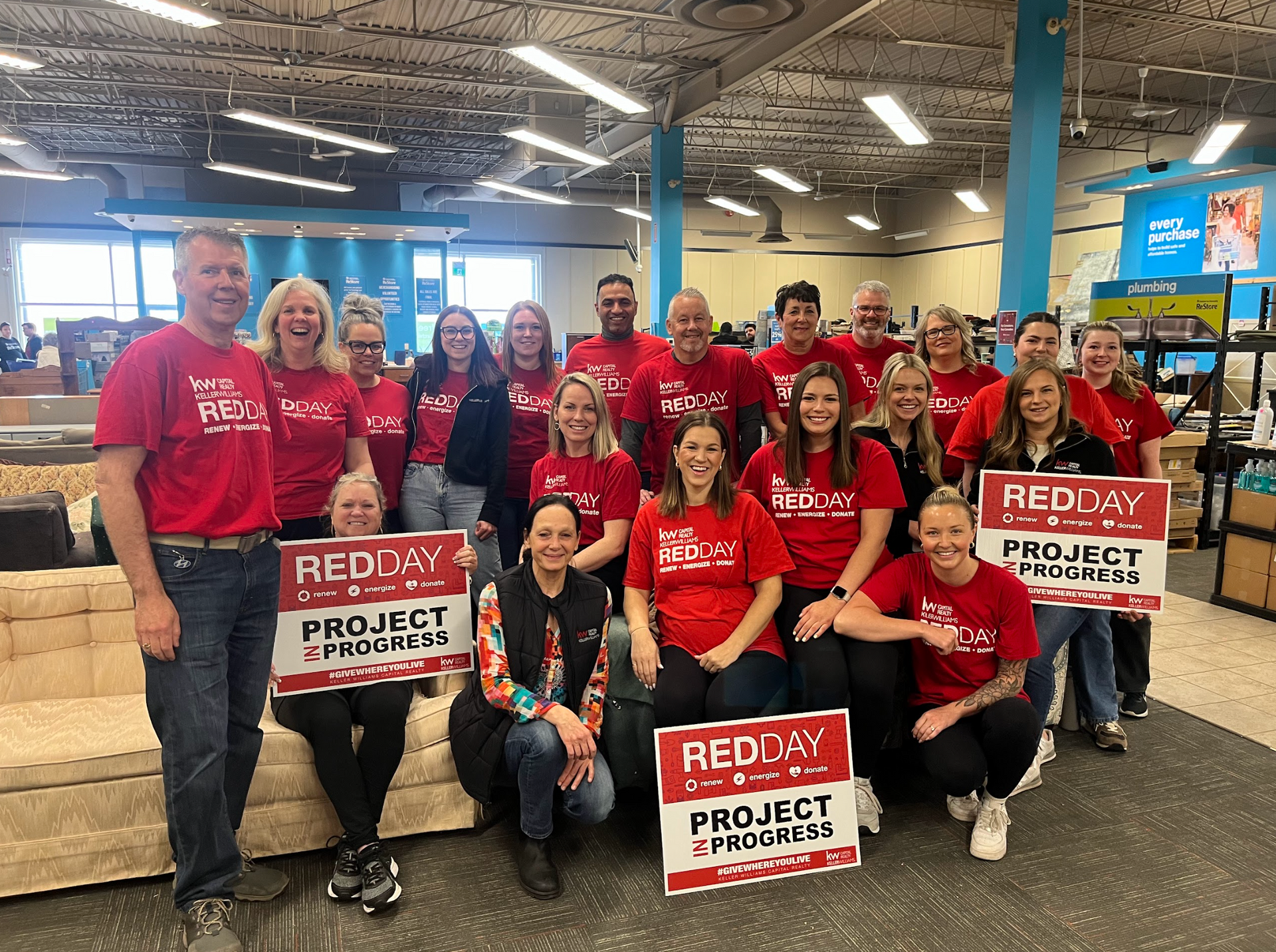 Habitat New Brunswick volunteers - Group in red shirts holding “REDDY Project” signs in a warehouse-like store.