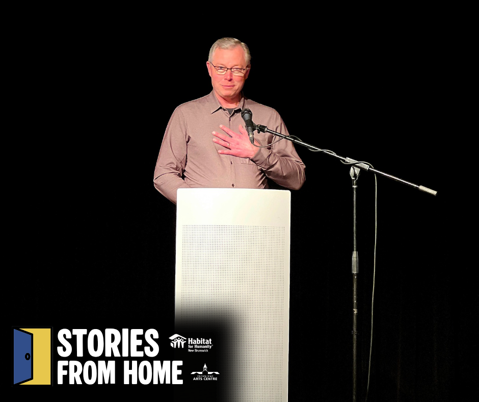 Perry speaking at a podium on a Habitat New Brunswick - dark stage during a Stories from Home event