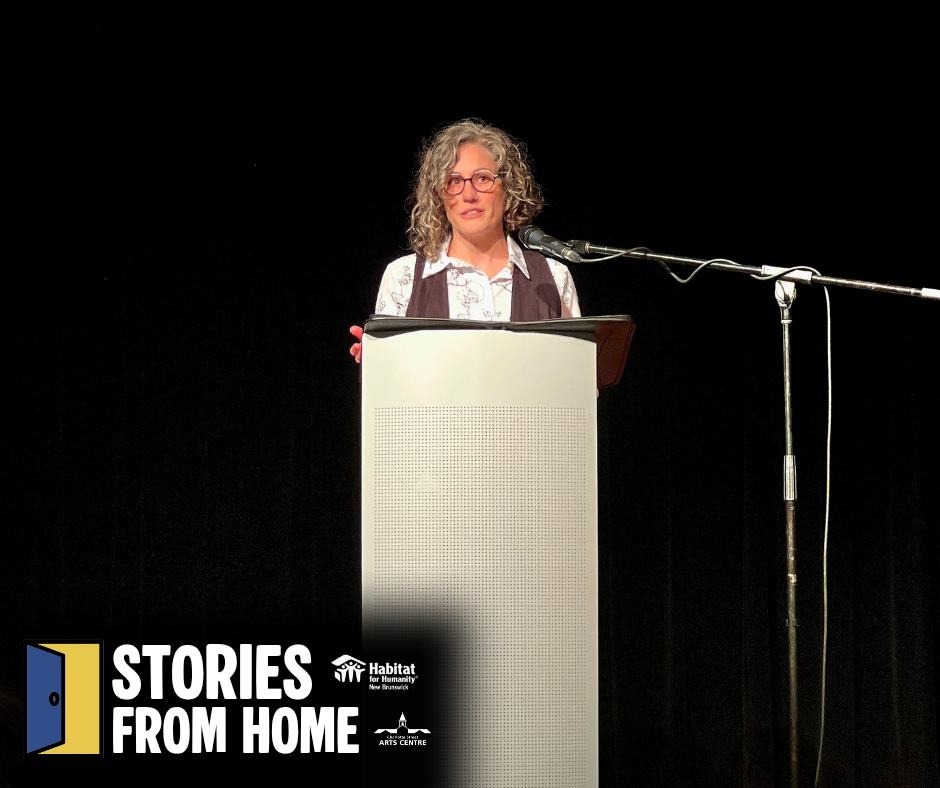 Habitat New Brunswick, Speaker at podium on stage with “Stories From Home” sign, addressing an audience under spotlight.