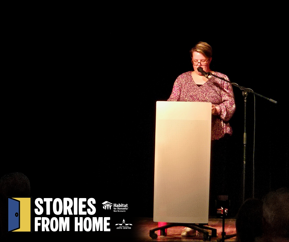 Habitat New Brunswick, Person speaking at a podium on a dark stage, with a Stories From Home logo in the corner.