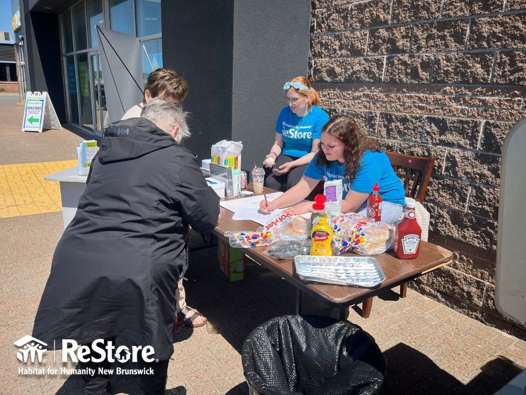 Habitat New Brunswick volunteers at a table outdoors sorting donated food and supplies near a ReStore truck
