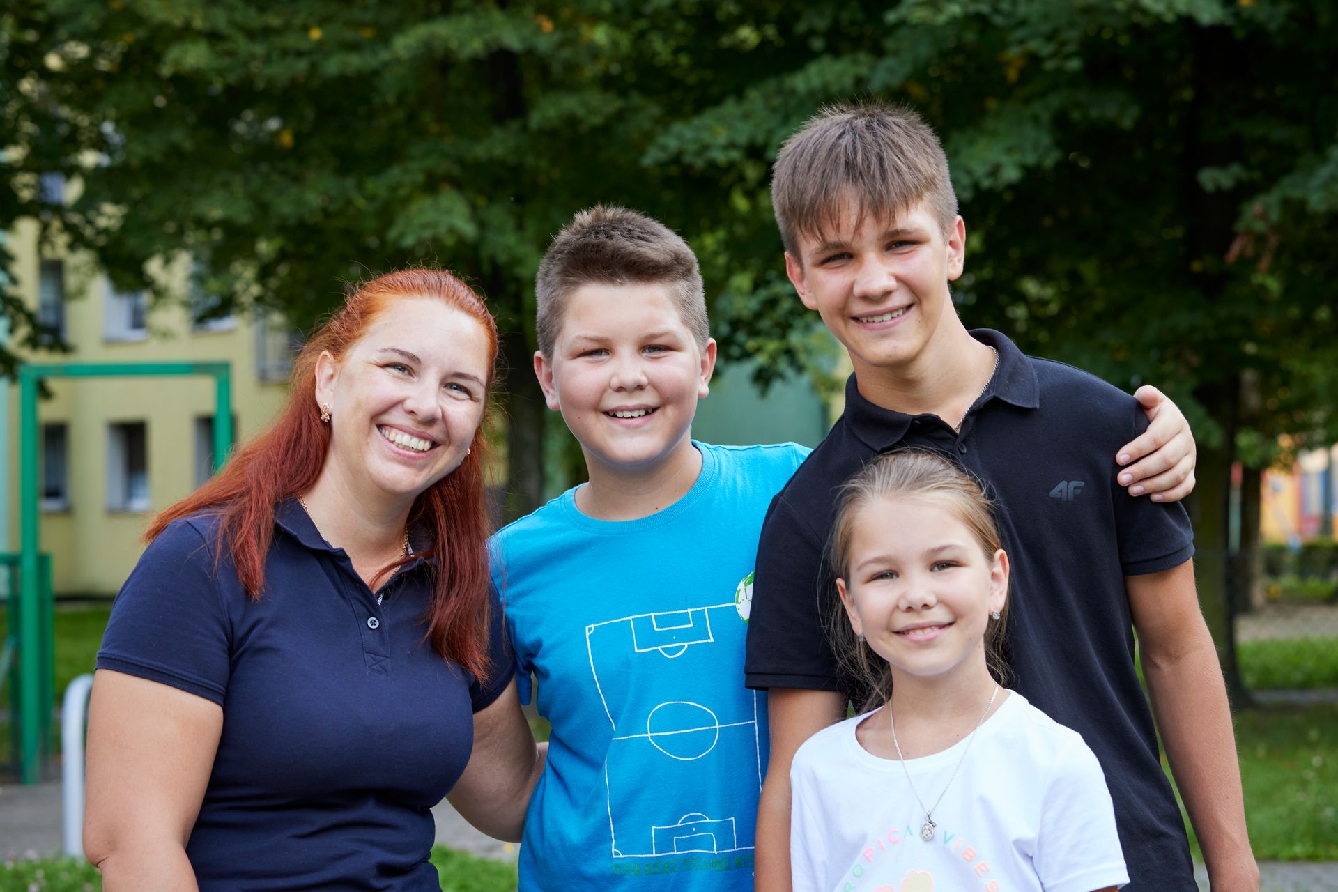Habitat New Brunswick partner family of 4 smiling standing together outdoors in a park, with trees and park in background