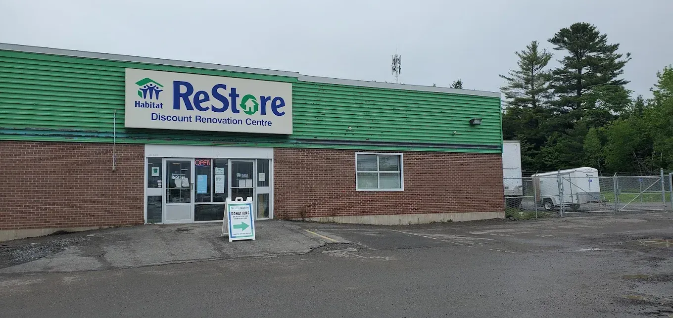 Fredericton ReStore thrift store storefront with green roof, brick walls, and parking lot in front