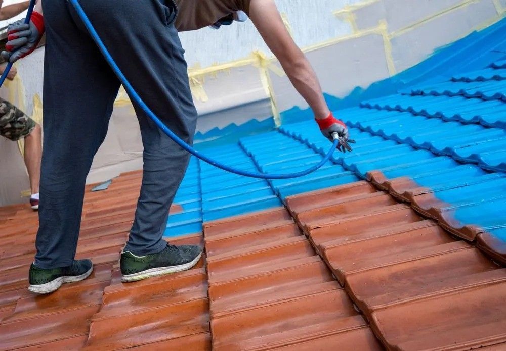 A Man is Spraying Blue Paint on a Tiled Roof — Roofpoint In Maryborough, QLD