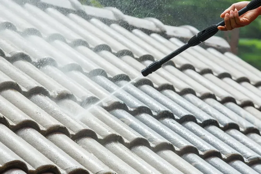A Person is Cleaning a Tiled Roof With a High Pressure Washer — Roofpoint In Maryborough, QLD