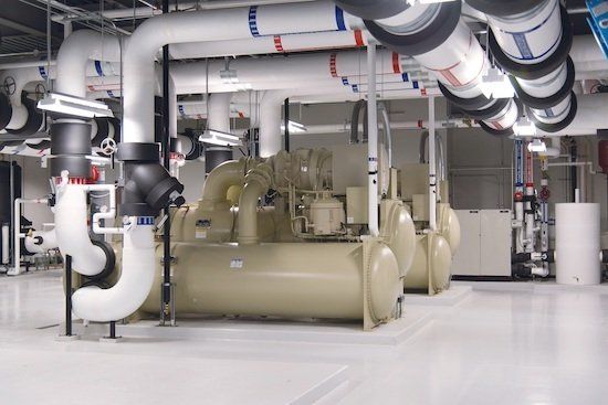 Large industrial chillers with white piping in an equipment room.