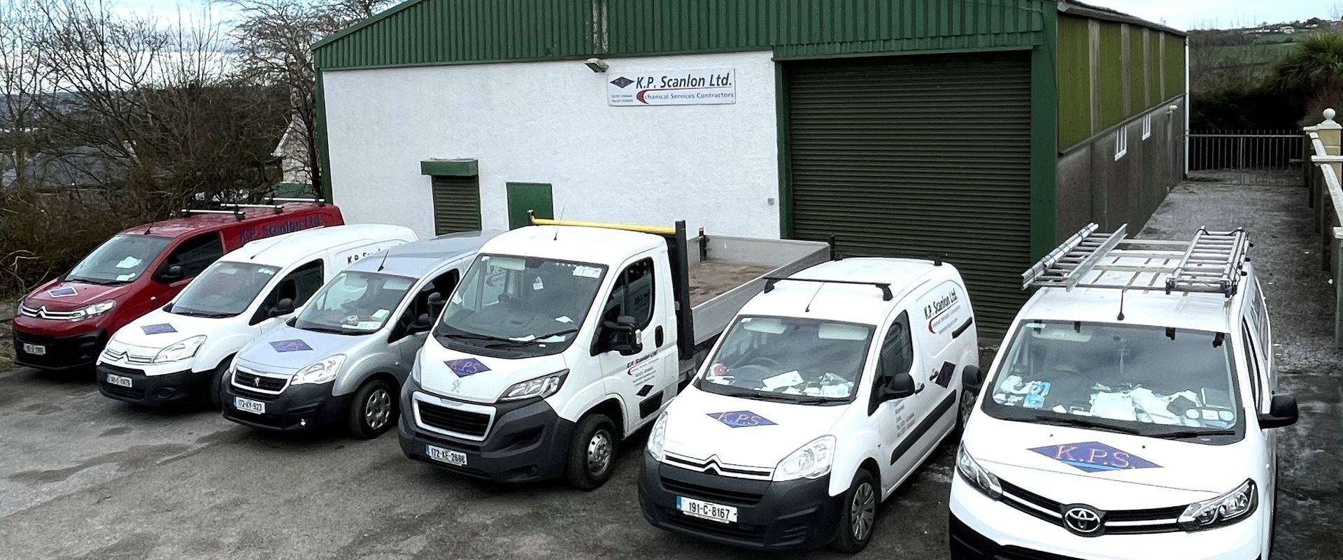 Several white vans parked in front of a white building with a green roof.