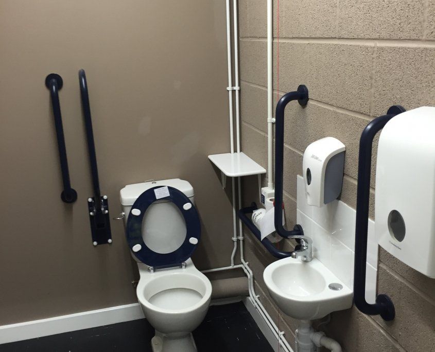 Accessible restroom with toilet, sink, grab bars, and paper towel dispenser.