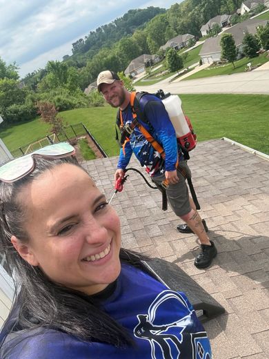 Two smiling people on a gravel path in a suburban neighborhood, one taking a selfie outdoors.