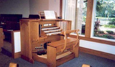 Organ with multiple keyboards and pedals in a room with a window overlooking a garden.