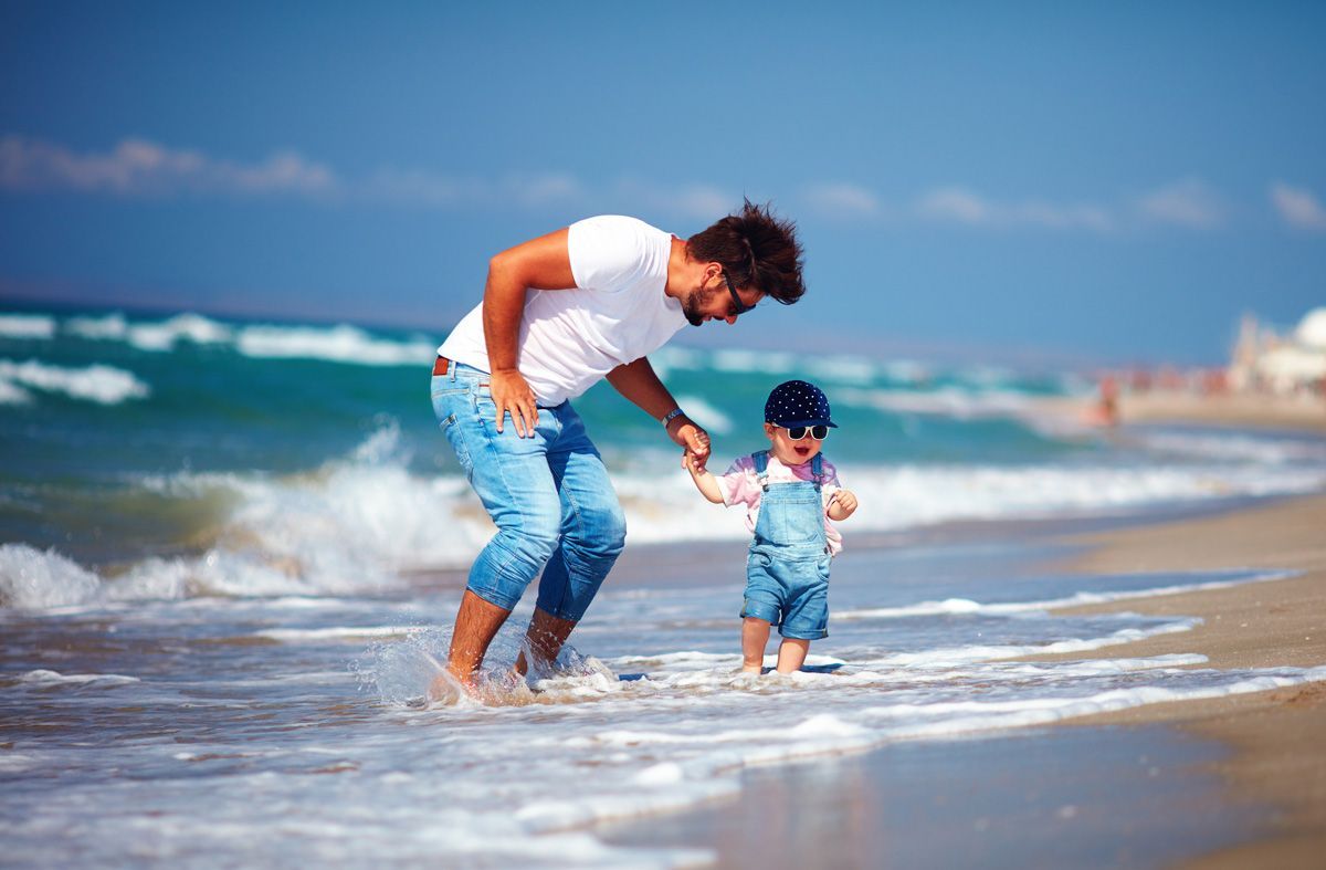 Adult helping child walk in shallow surf on a sunny beach