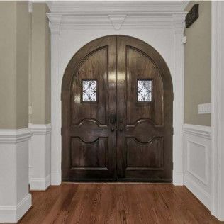 Dark wooden double doors with arched top and decorative windows, set in a white-trimmed doorway.