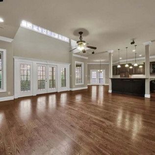 Spacious, empty living room with hardwood floors, white doors, and a dark island with pendant lights.