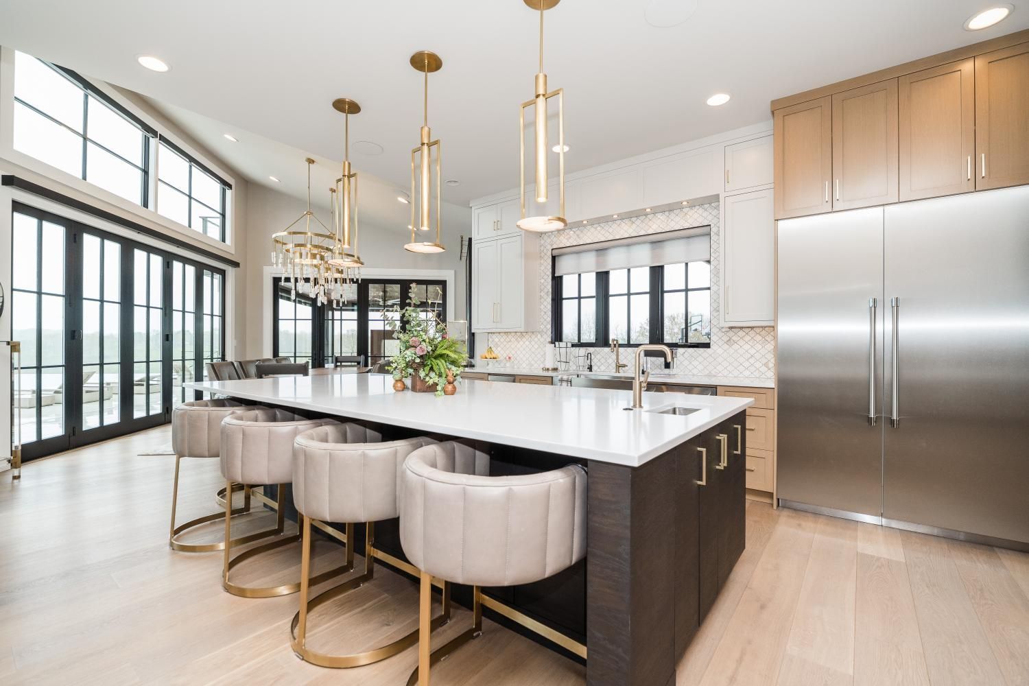 Bright modern kitchen with large island, beige stools, brass pendants, and stainless steel appliances