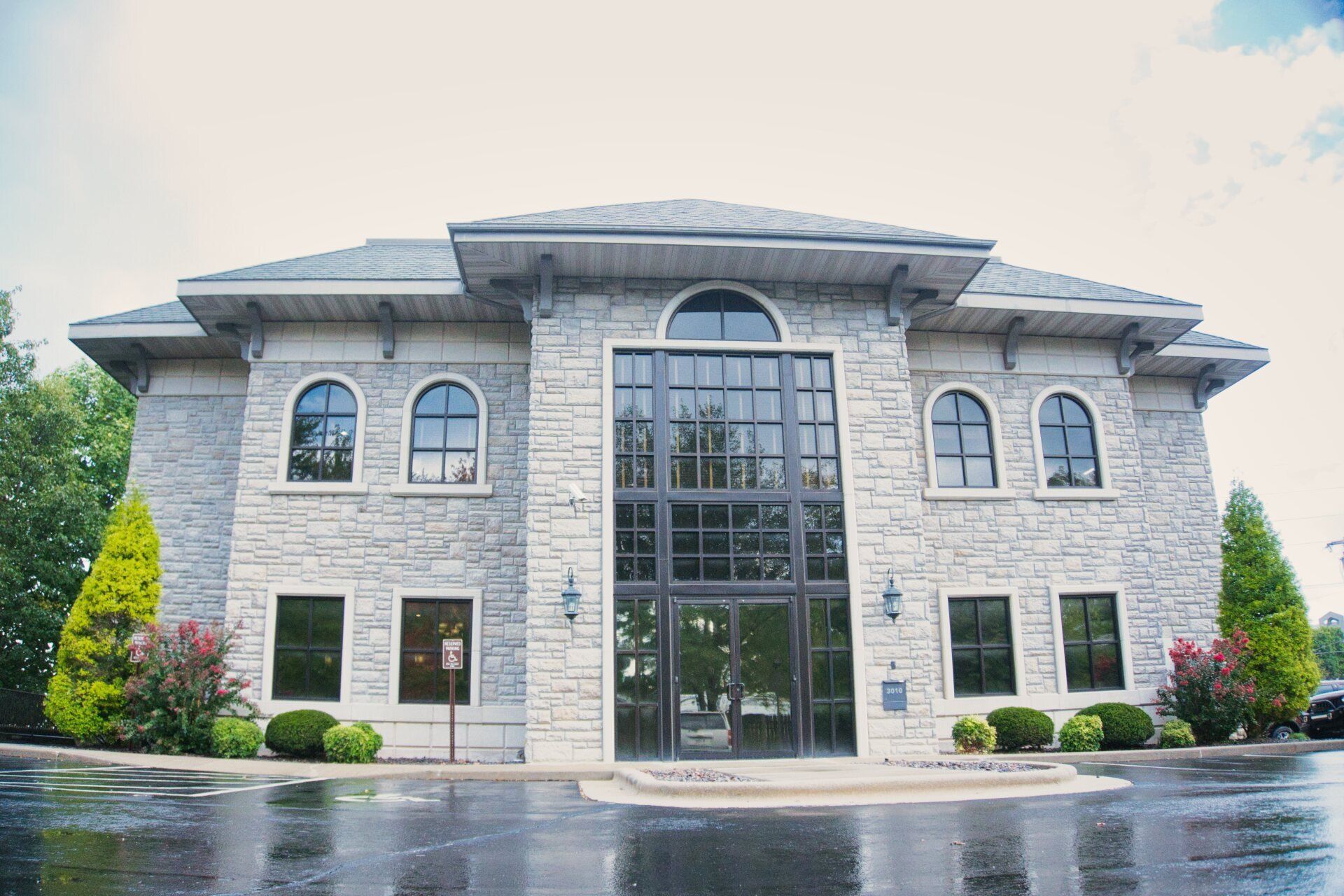 Large stone building with arched windows and a central glass entrance on a wet driveway