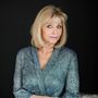 Portrait of a blonde woman in a blue patterned blouse against a black background