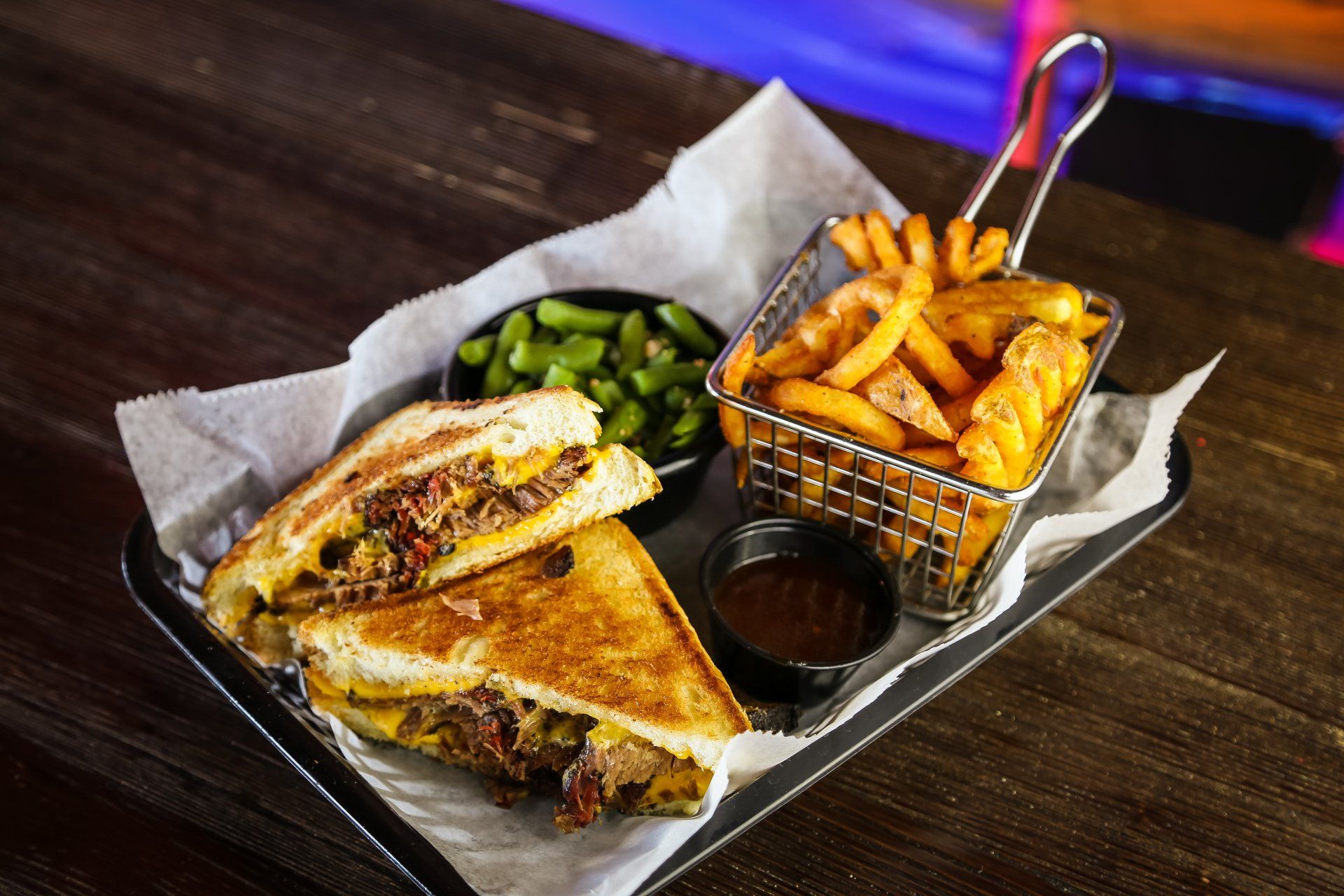 Grilled sandwich with fries, broccoli, and dipping sauce on a tray