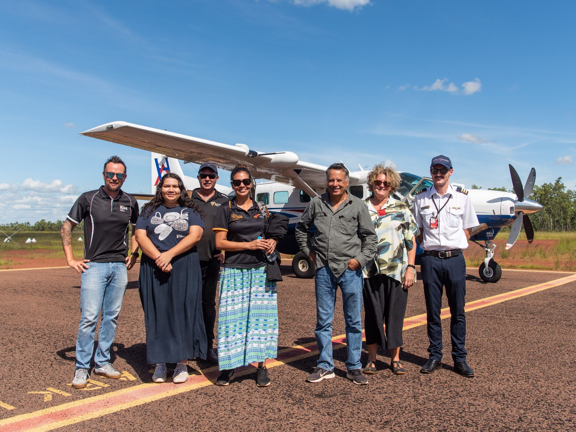 Steve Goat standing with group of people  on remote airstrip in NT in front of a light aircraft. 