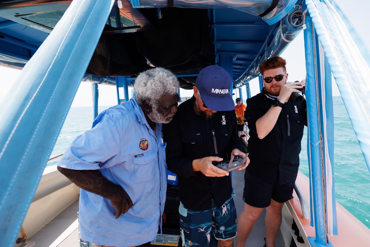 Steve Goat standing with Tiwi Island Rangers on a boat looking at drone control as they survey ocean for ghost nets.