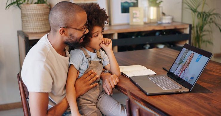 Adult and child sitting at a table, looking at a laptop in a home living room