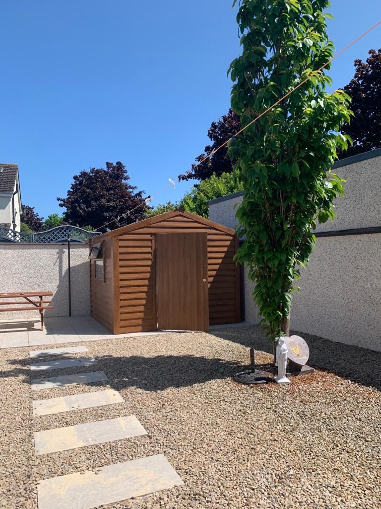 Brown shed in a gravel yard with a tree and stepping stones under a blue sky.