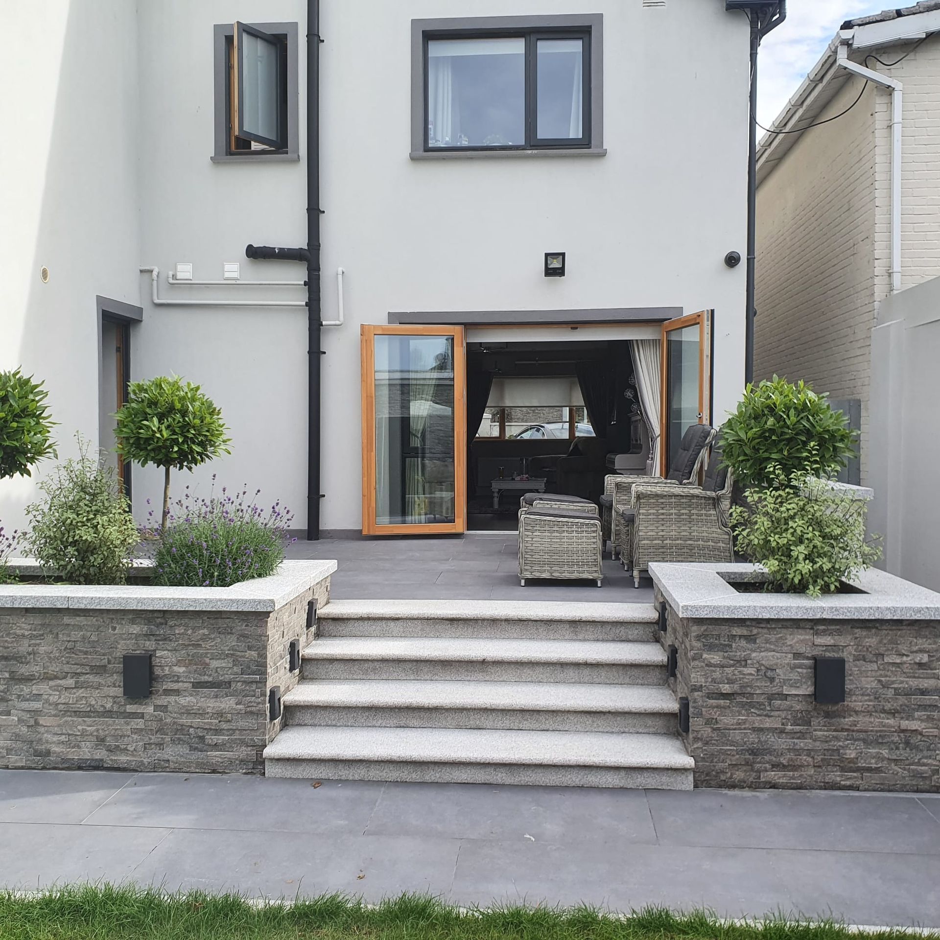 Backyard patio with steps, planters, and a home's rear exterior featuring a door and windows.