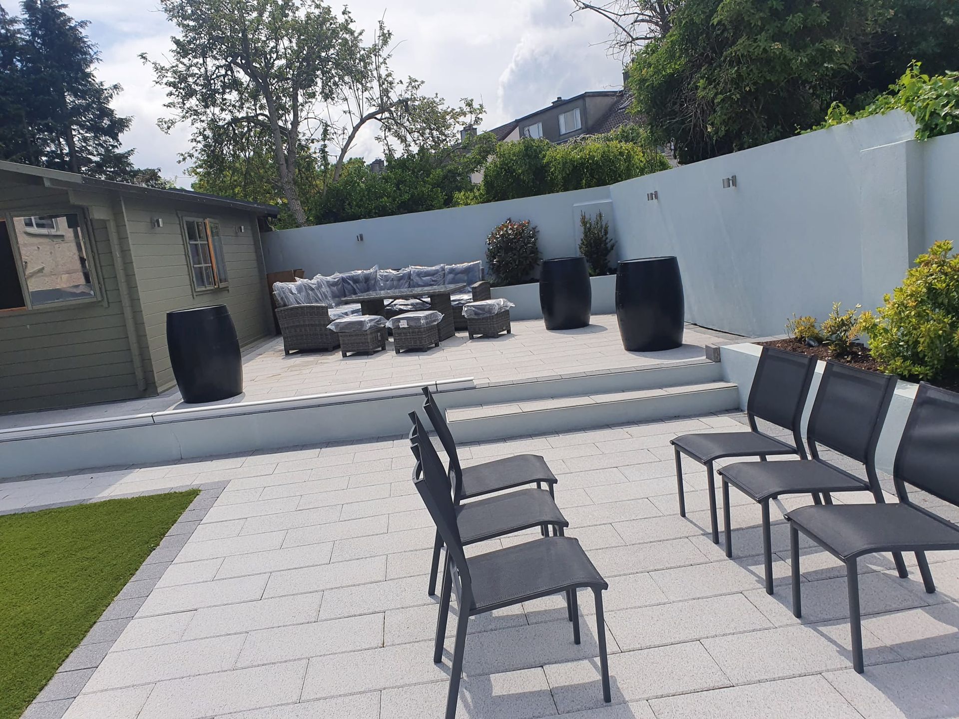 Patio with seating areas: chairs, sofa, dark planters, and a small wooden shed.