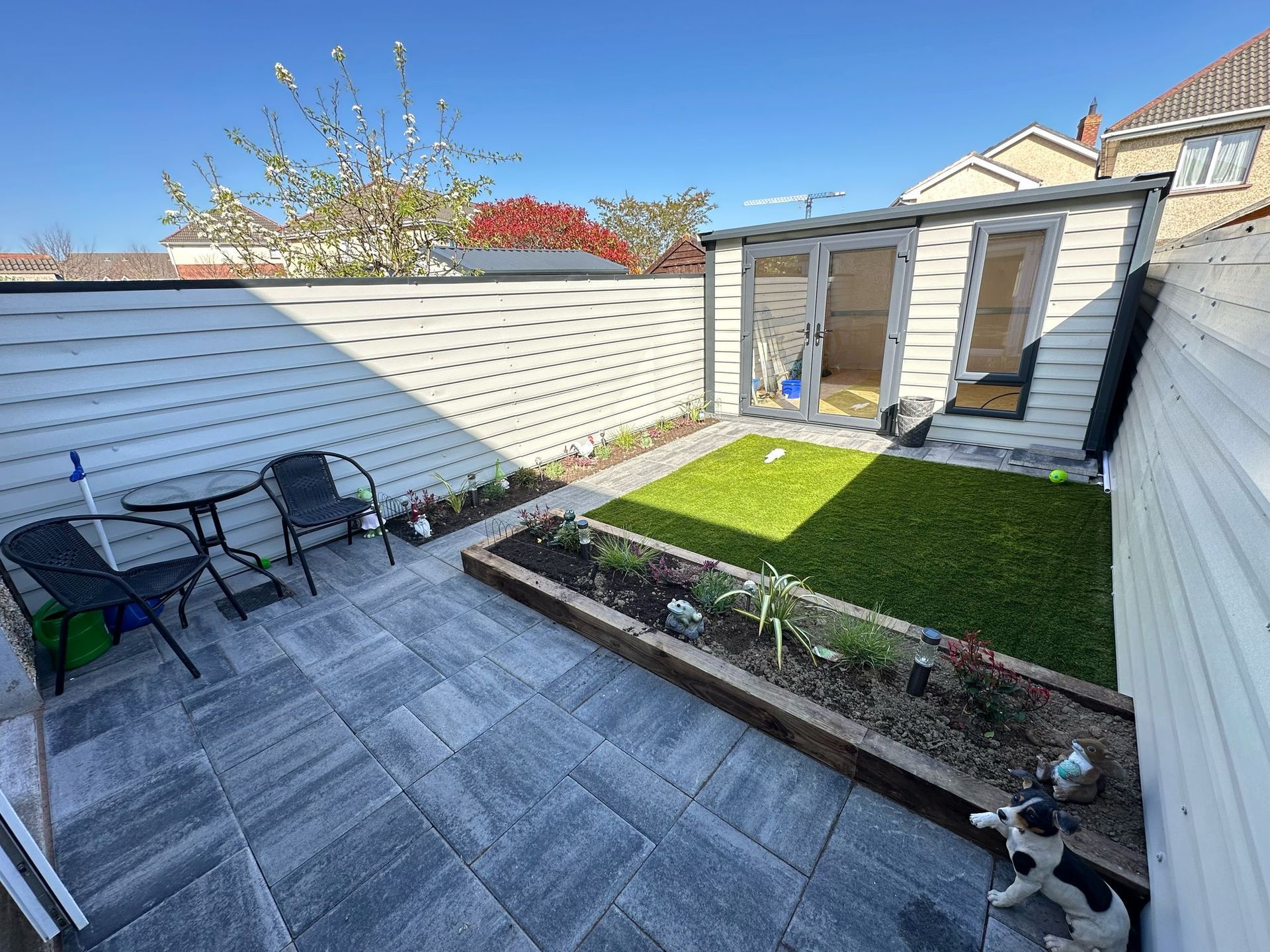 Small backyard patio with gray pavers, grass patch, shed, and dog.