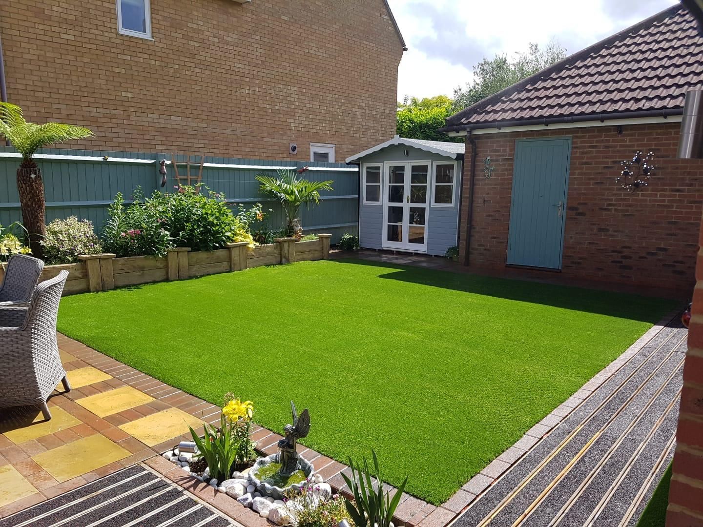 A backyard with green artificial turf, a shed, and a patio, surrounded by a wooden border.