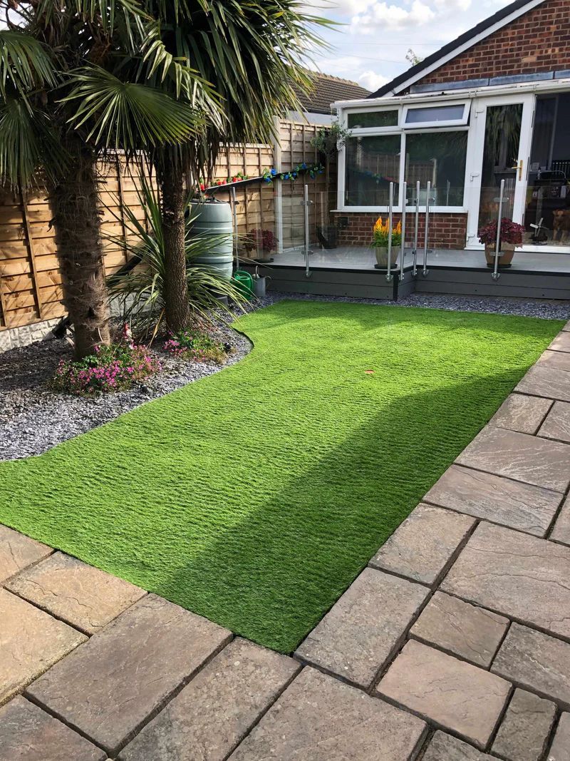 Backyard with artificial green turf, palm trees, stone patio, and brick house.