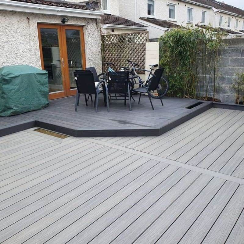 Gray composite deck with a seating area, brown double doors, and a covered grill.