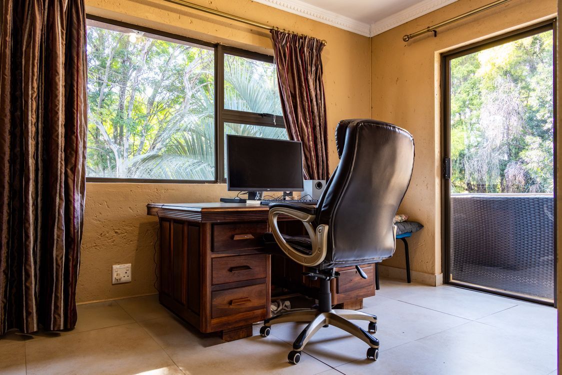 Home office desk and computer beside large windows overlooking a leafy garden