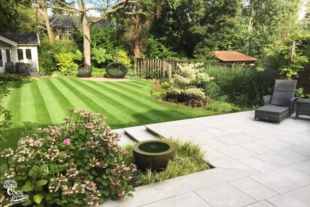 Lush backyard with manicured lawn, stone patio, and various plants, with seating area and shed.