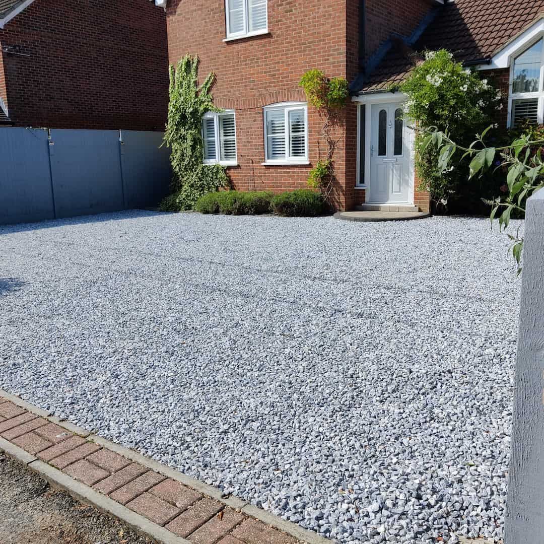 Gravel driveway in front of a brick house with a white door and windows.