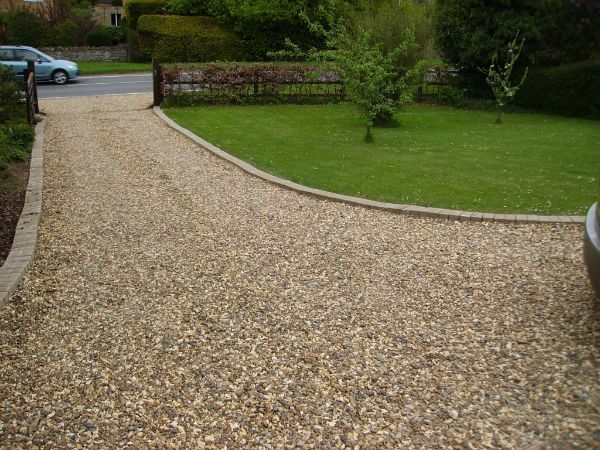 Gravel driveway leading to a grassy lawn, with a car parked on the right and a street in the background.