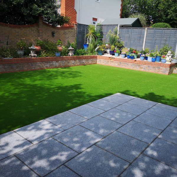 A backyard with a patio, green lawn, brick walls, and potted plants.