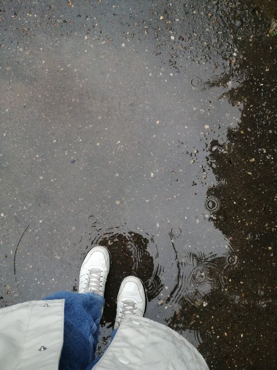 Person standing in a rain puddle on wet paving