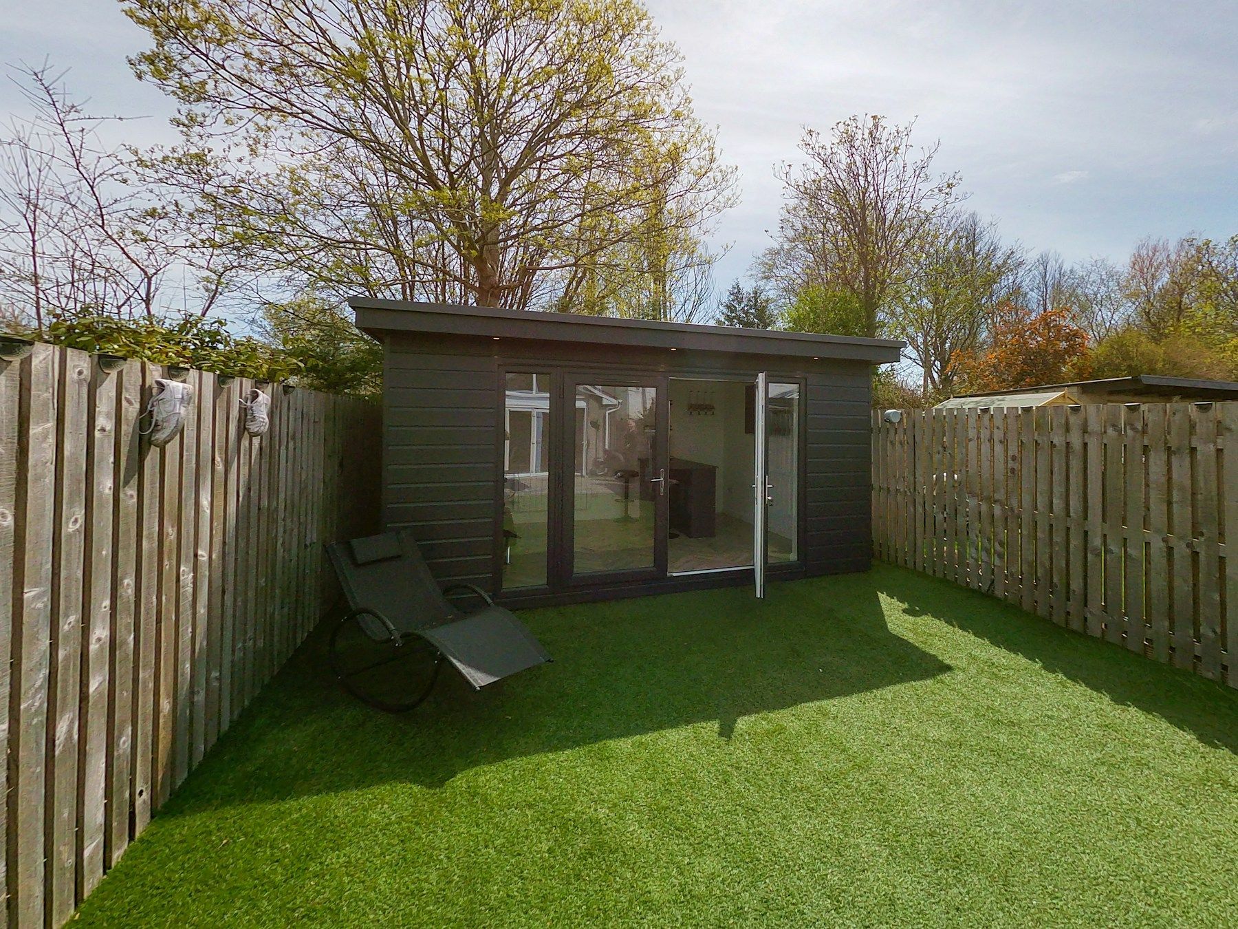 Modern dark-clad garden room with glazed double doors in a fenced back garden