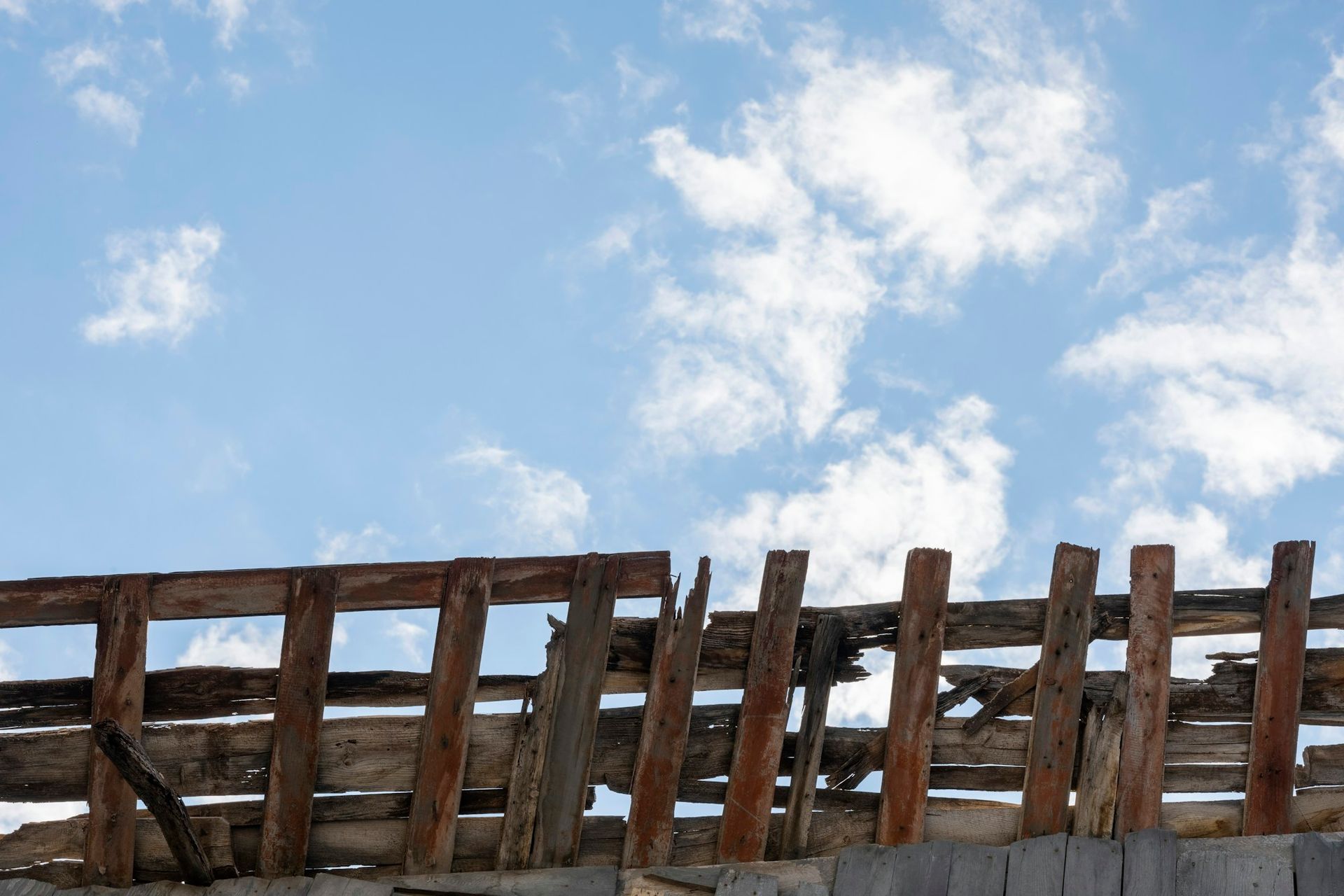 Broken and weathered wooden fence beneath a cloudy blue sky