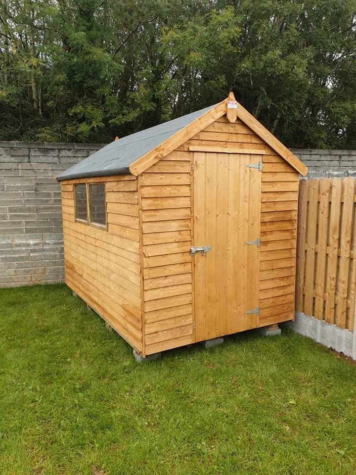 Wooden shed with a pitched roof, window, and door, set on a grassy lawn.