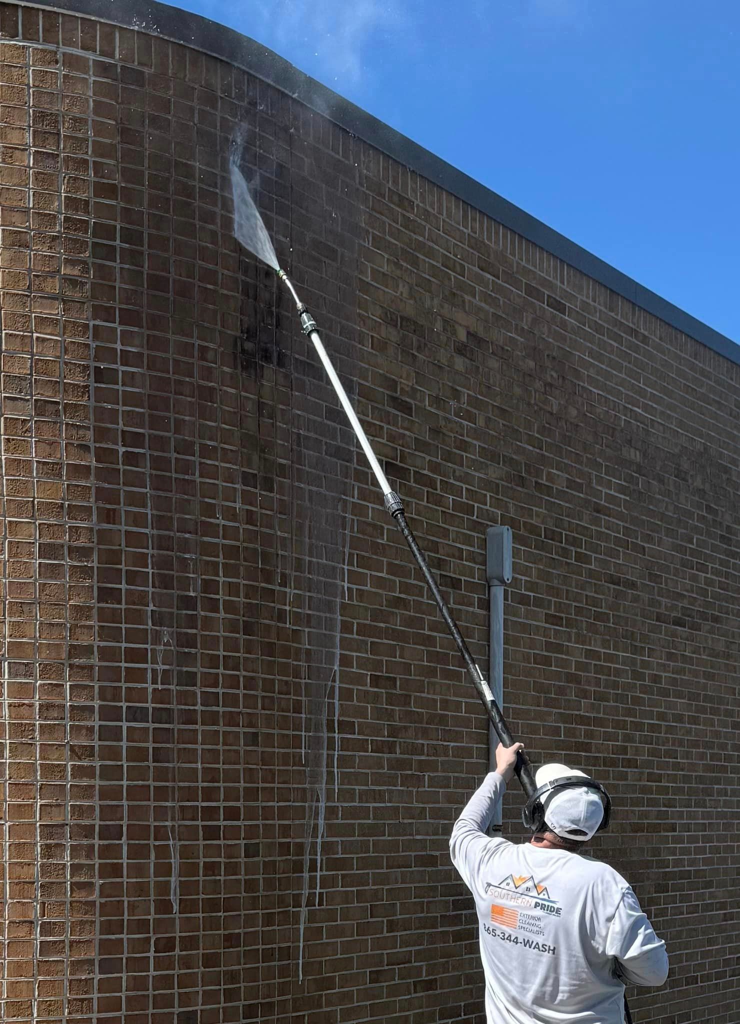 A man is cleaning a brick wall with a high pressure washer.