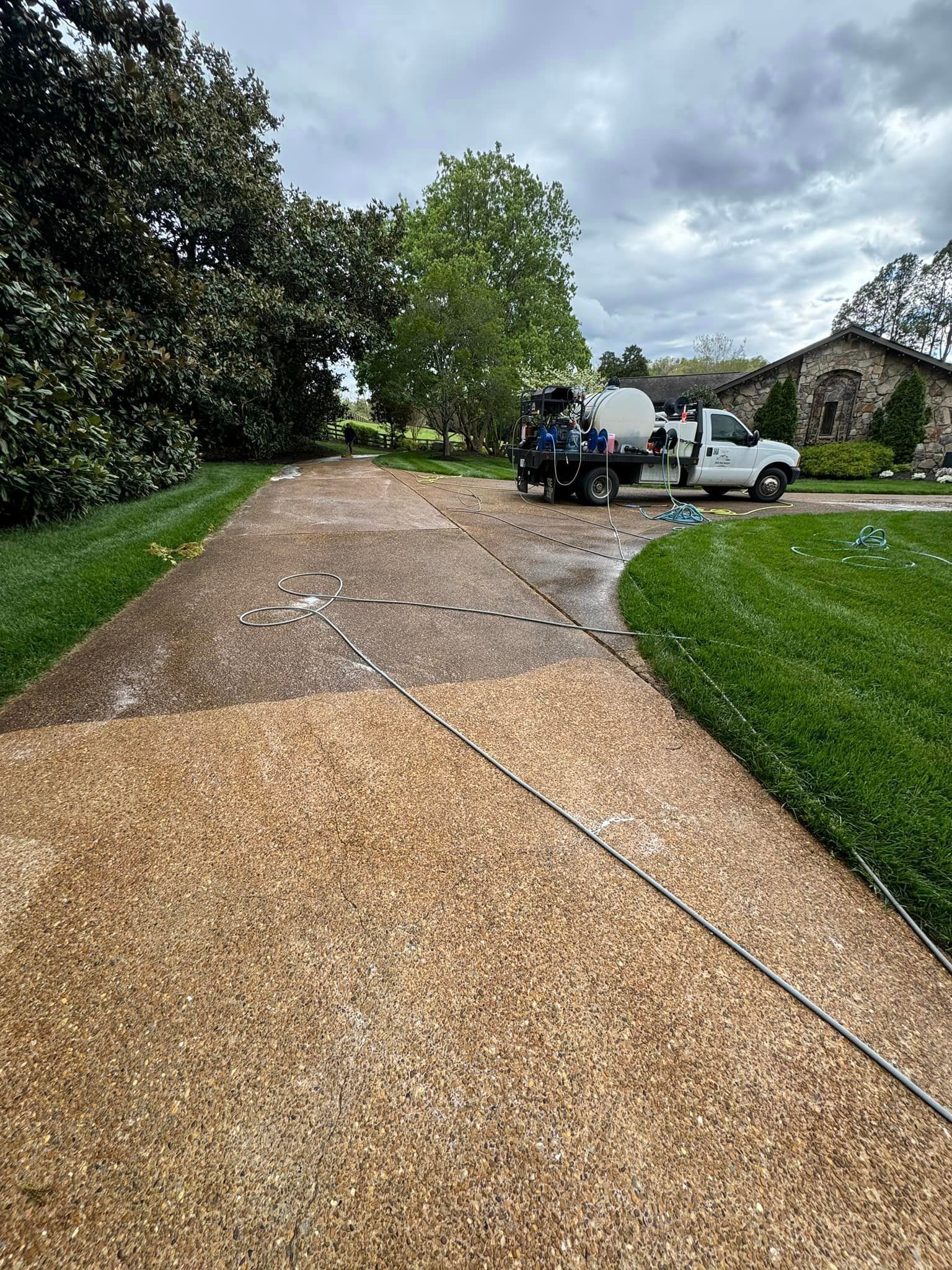 A white truck is washing a driveway next to a house.