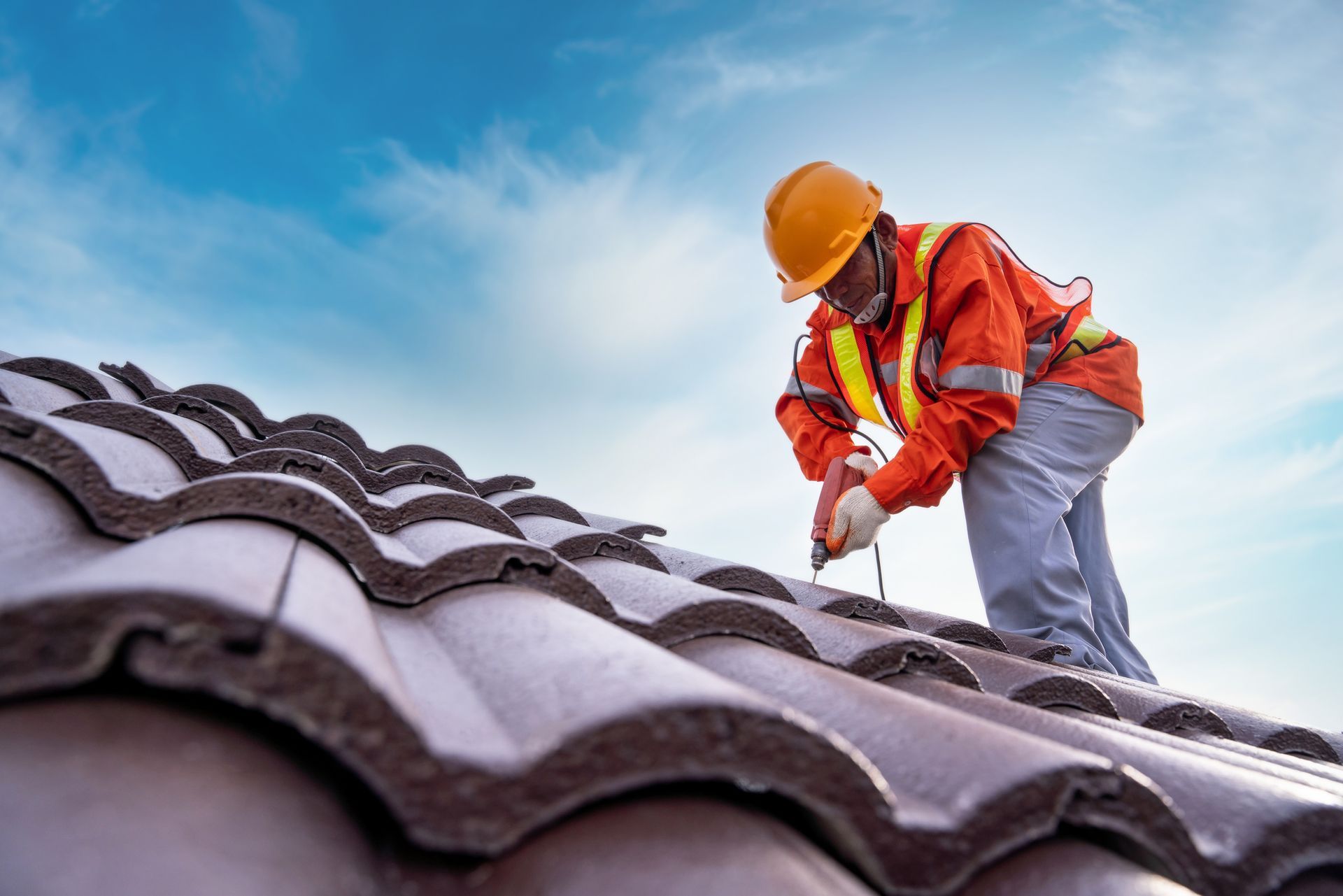 A roofer drills into a steel roof during installation by a residential roofing contractor service.