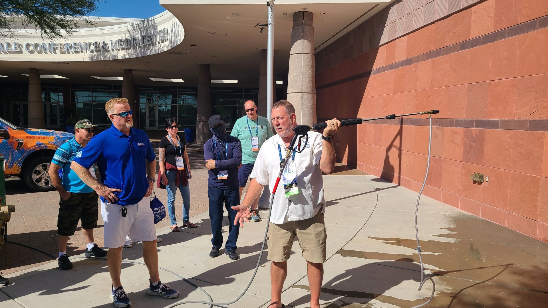 People standing outside a building entrance in bright sunlight, with one man carrying a camera.