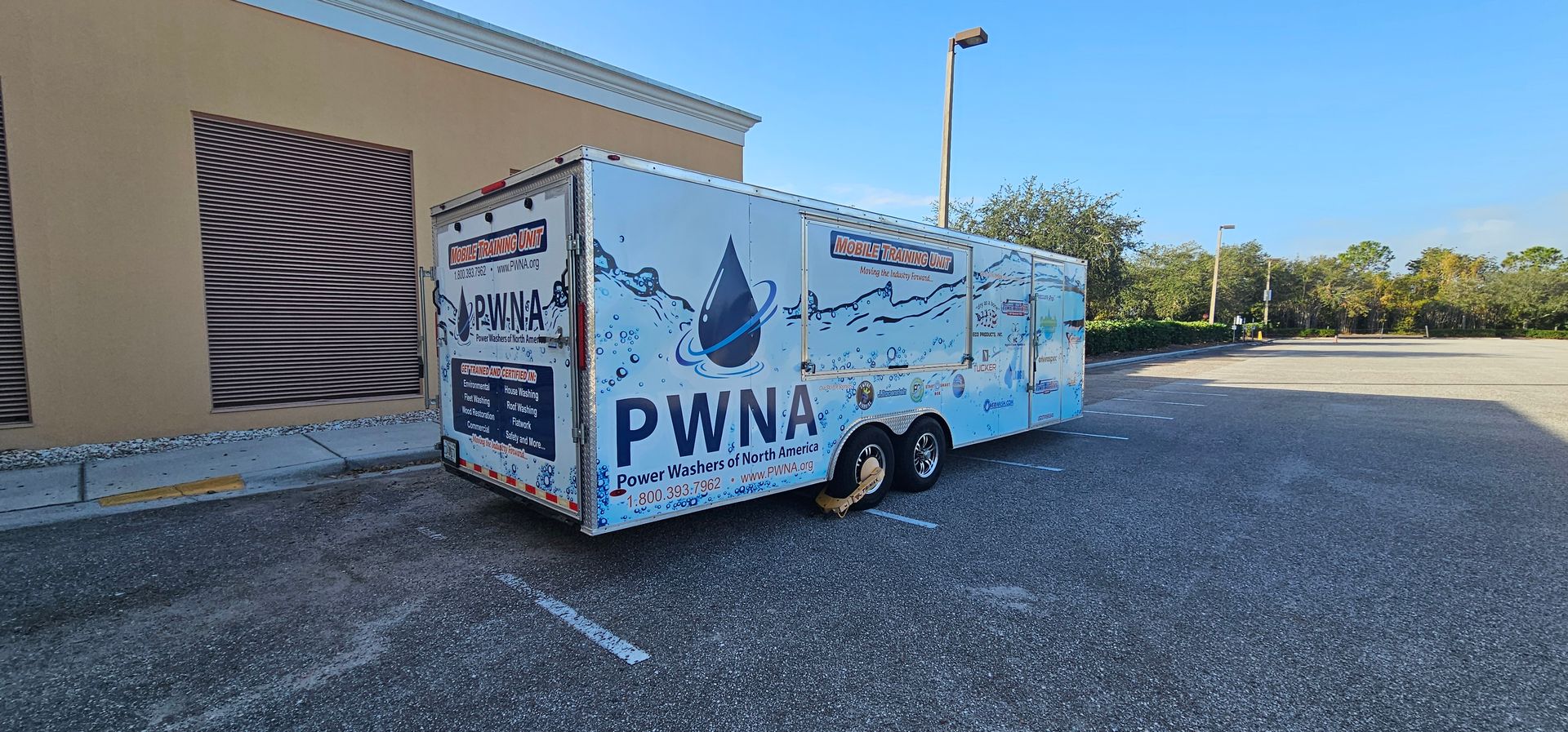 Blue PWNA-branded trailer parked beside a tan building on a sunny day.