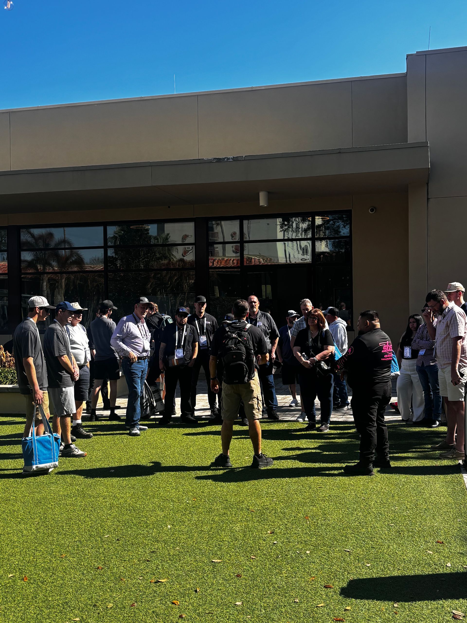 Group of people gathered on a grassy lawn outside a building on a sunny day.