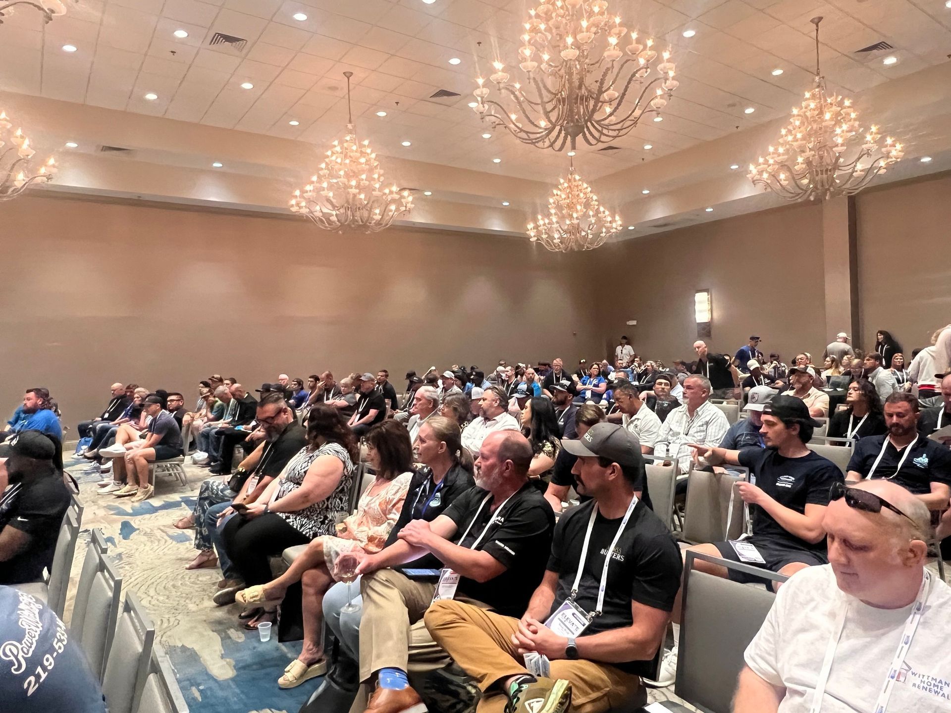 Audience seated in a conference room under chandeliers, listening to a presentation