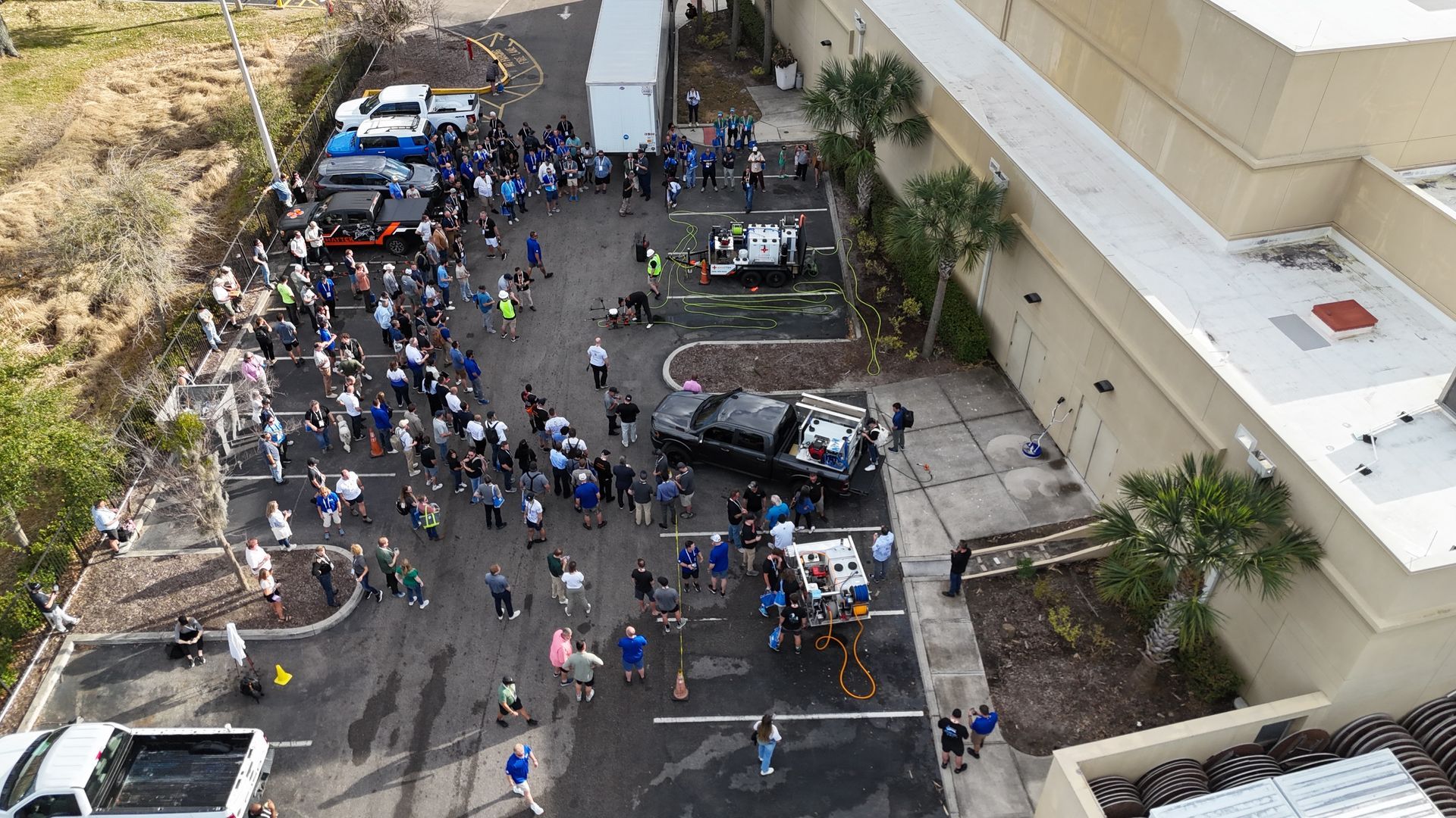 Crowd gathered around emergency vehicles and tents in a parking lot beside a building